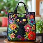 Bolso tote acolchado negro con gato negro entre flores multicolores